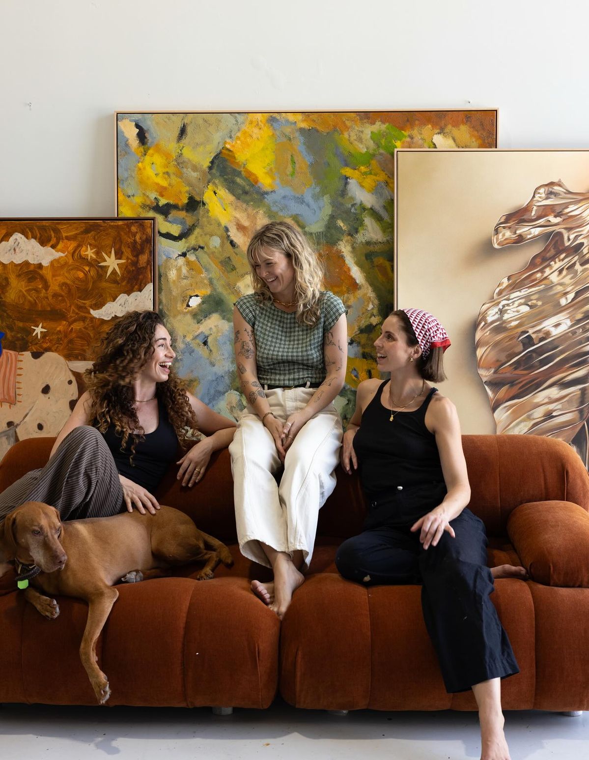 Три подруги на диване в студии с картинами